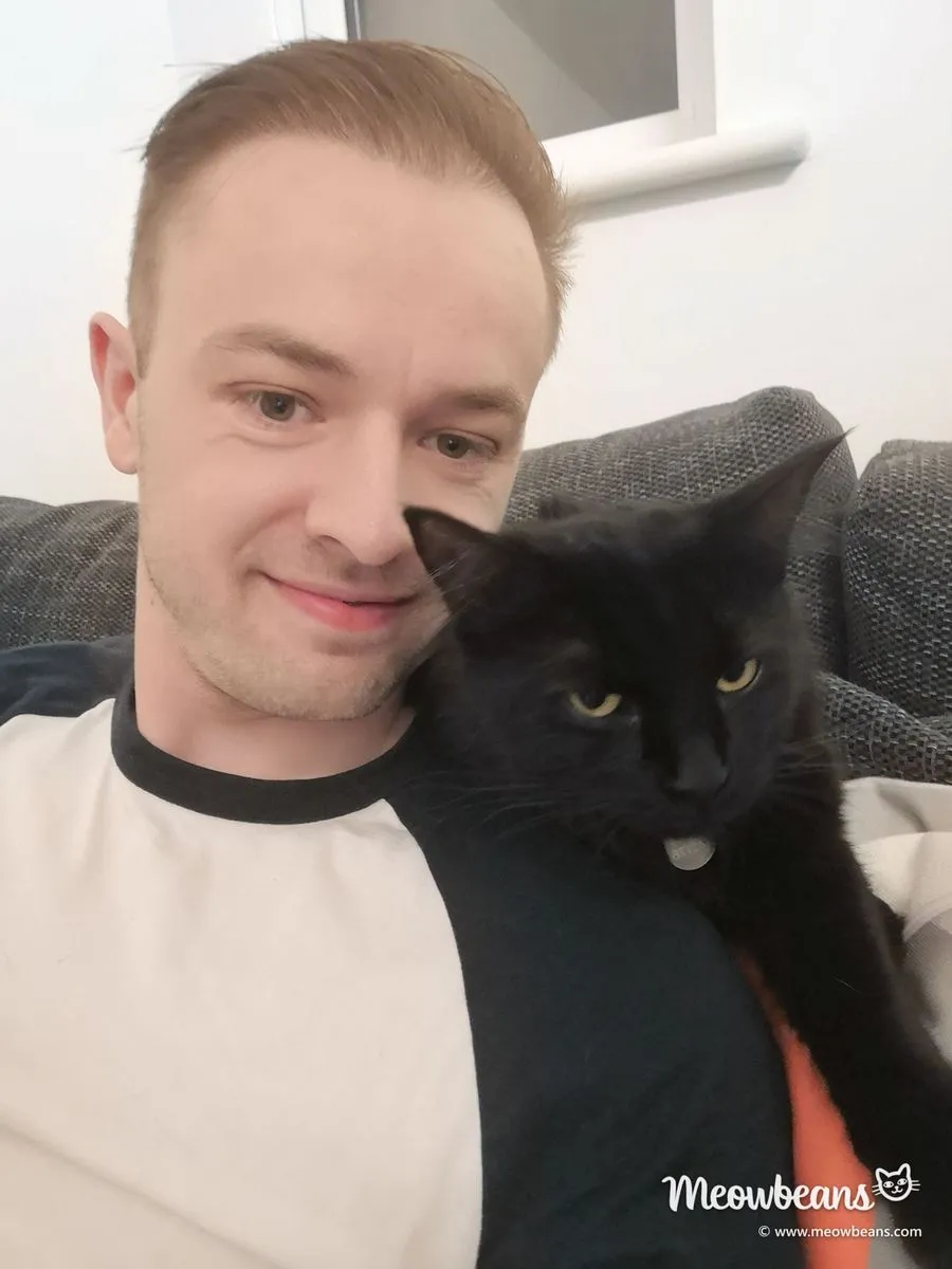 John on the sofa with Mila, his black cat, on his shoulder